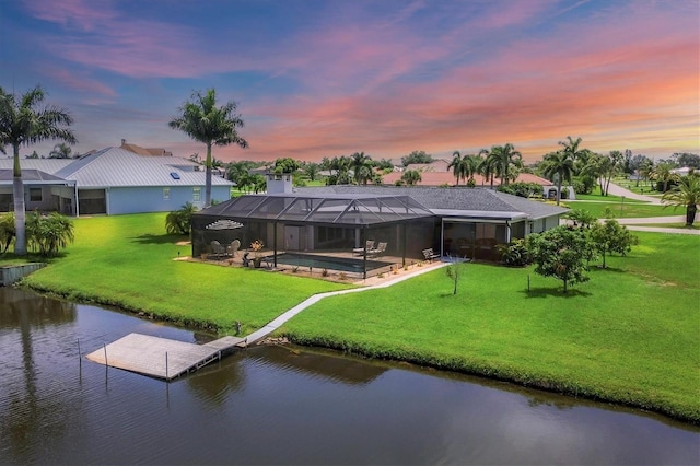 back house at dusk featuring a lawn, glass enclosure, a pool, and a water view