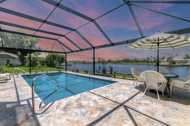 pool at dusk featuring glass enclosure, a water view, and a patio area