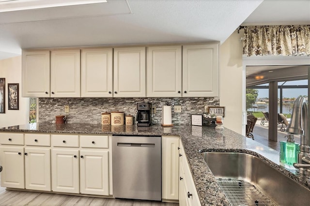 kitchen with tasteful backsplash, sink, dishwasher, dark stone countertops, and light hardwood / wood-style flooring