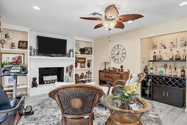 living room featuring light wood-type flooring, bar area, a large fireplace, and ceiling fan