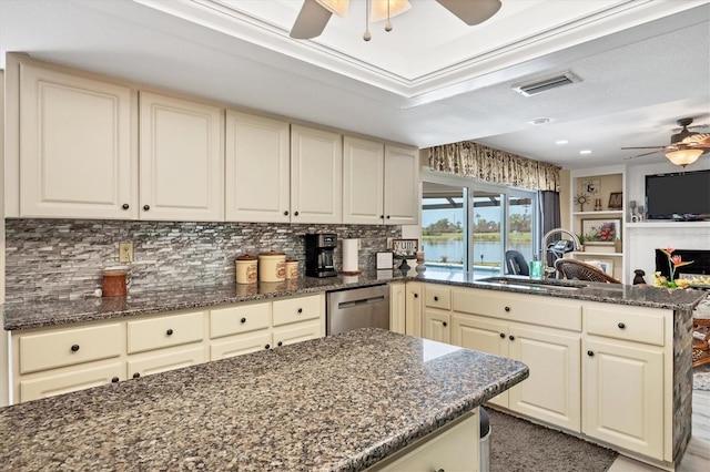 kitchen with dark stone countertops, stainless steel dishwasher, sink, and cream cabinets