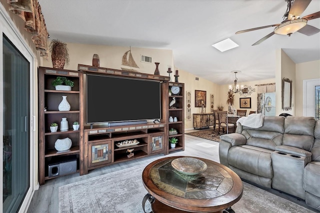 living room featuring lofted ceiling with skylight, hardwood / wood-style floors, and ceiling fan with notable chandelier