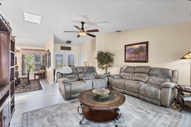 living room with light wood-type flooring, ceiling fan, and lofted ceiling with skylight