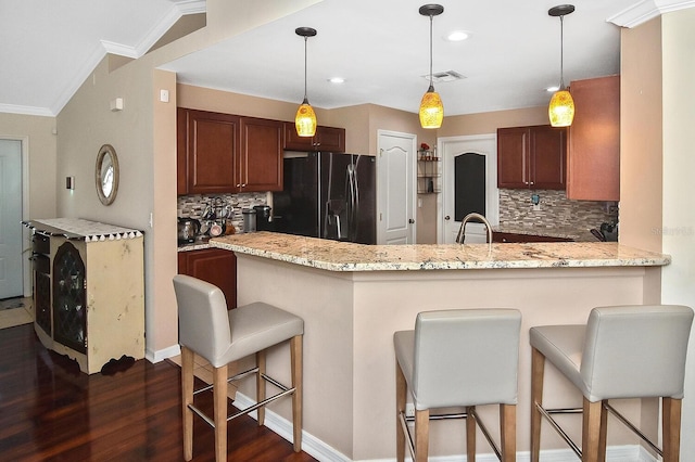 kitchen with black fridge, dark hardwood / wood-style flooring, a breakfast bar area, and tasteful backsplash