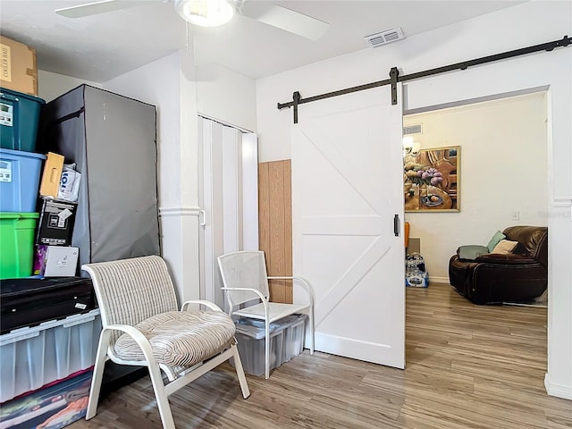 living area with light hardwood / wood-style flooring, a barn door, and ceiling fan