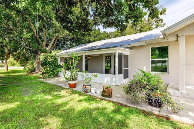 view of home's exterior with a sunroom, a lawn, and stucco siding