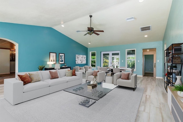 living area featuring arched walkways, light wood finished floors, visible vents, ceiling fan, and high vaulted ceiling