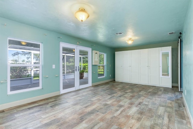 unfurnished bedroom with light wood-type flooring, a barn door, access to outside, and french doors