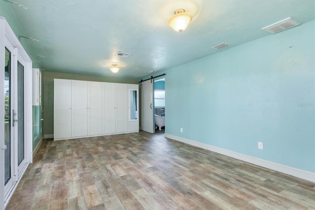 unfurnished bedroom featuring a barn door, a closet, and light hardwood / wood-style floors