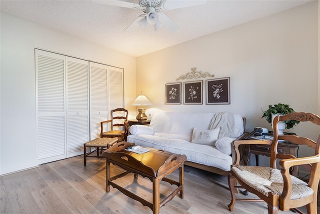 living room with a textured ceiling, ceiling fan, and light hardwood / wood-style floors