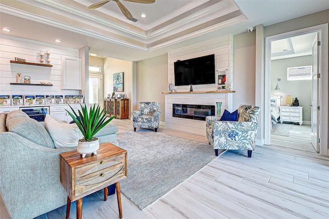 living room featuring ceiling fan, ornamental molding, a tray ceiling, and light hardwood / wood-style flooring