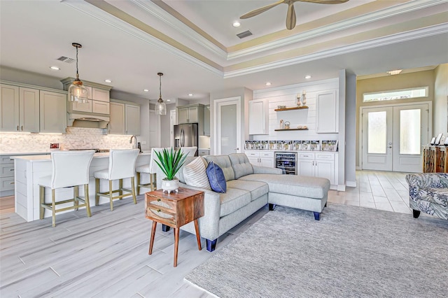 living room featuring indoor wet bar, beverage cooler, a raised ceiling, crown molding, and french doors