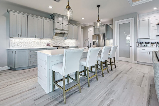 kitchen featuring hanging light fixtures, gray cabinets, a kitchen breakfast bar, and appliances with stainless steel finishes