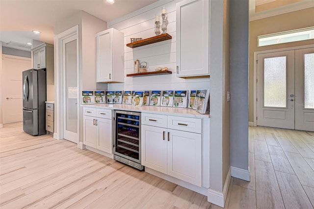 bar with wine cooler, white cabinetry, light wood-type flooring, and stainless steel refrigerator