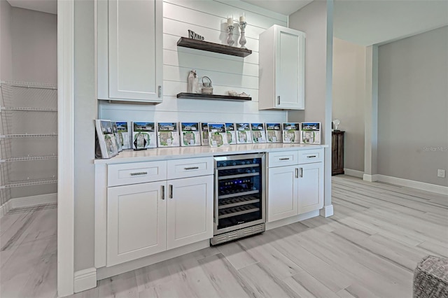 bar with wine cooler, light wood-type flooring, and white cabinets