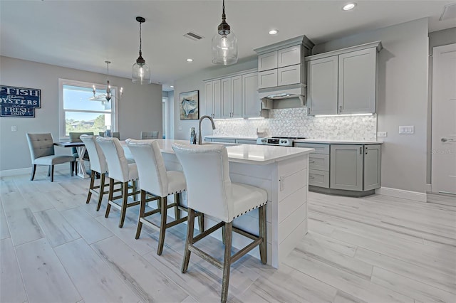 kitchen with a breakfast bar area, range, gray cabinetry, a center island with sink, and decorative light fixtures