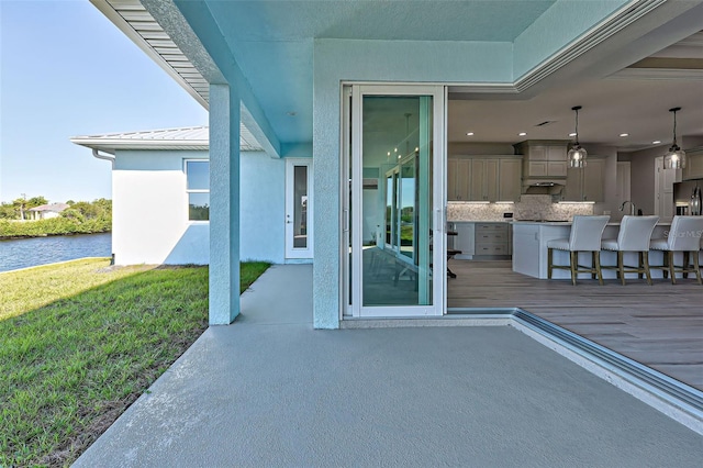 view of exterior entry with a water view, exterior bar, and a lawn