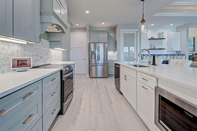 kitchen with pendant lighting, sink, stainless steel appliances, custom exhaust hood, and light wood-type flooring