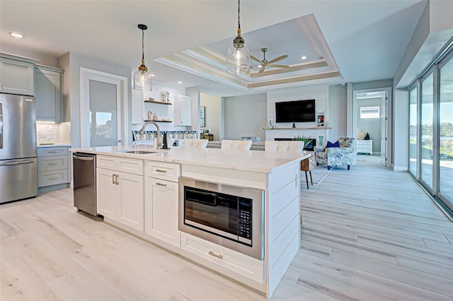 kitchen with built in microwave, hanging light fixtures, stainless steel refrigerator, a raised ceiling, and a kitchen island with sink