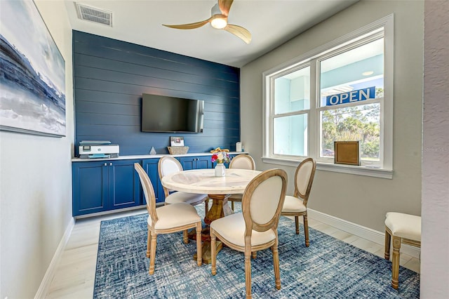 dining area featuring wooden walls, ceiling fan, and light wood-type flooring