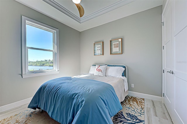 bedroom with crown molding, ceiling fan, a water view, light hardwood / wood-style floors, and a raised ceiling