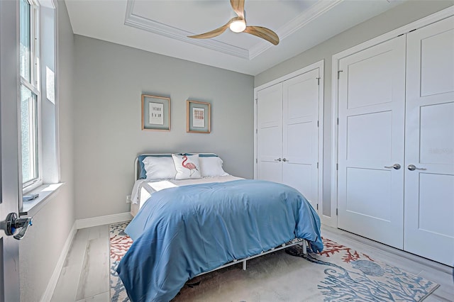 bedroom featuring multiple closets, ceiling fan, crown molding, and light hardwood / wood-style flooring