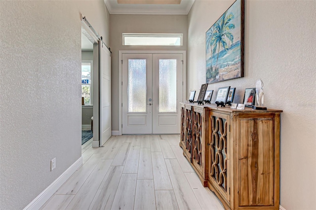 entryway featuring crown molding, a barn door, light wood-type flooring, and french doors