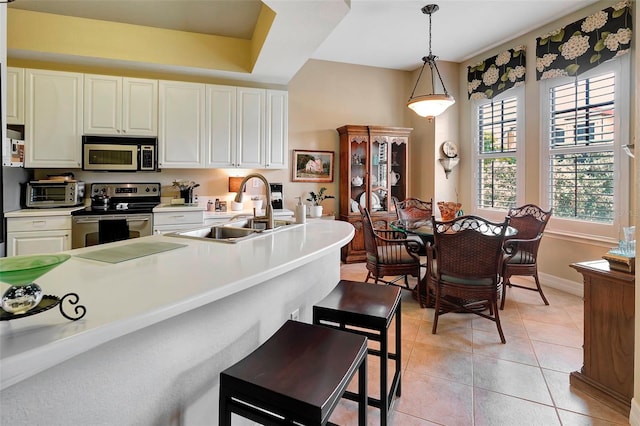 kitchen featuring a kitchen breakfast bar, sink, decorative light fixtures, appliances with stainless steel finishes, and light tile patterned floors