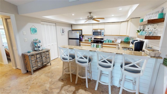 kitchen featuring a tray ceiling, ceiling fan, white cabinets, and stainless steel appliances