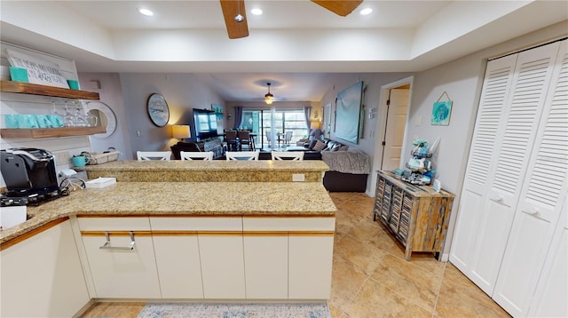 kitchen featuring white cabinets, light stone counters, ceiling fan, light tile patterned floors, and a tray ceiling