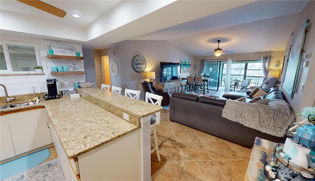 kitchen with light tile patterned flooring, a breakfast bar area, kitchen peninsula, white cabinets, and ceiling fan