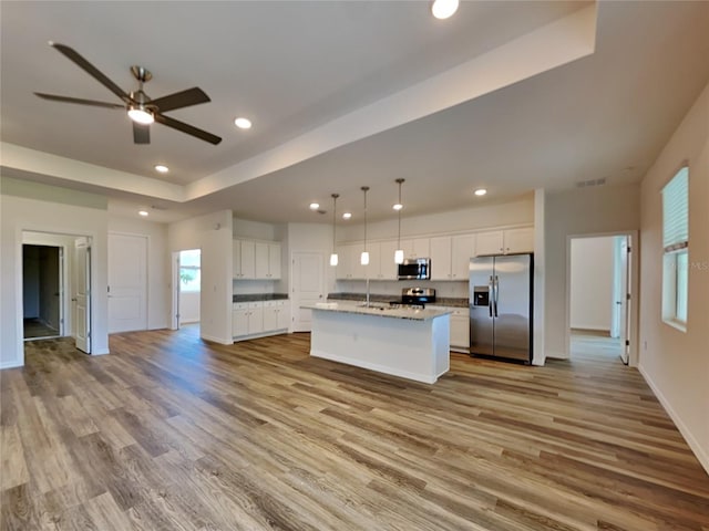 kitchen featuring white cabinets, stainless steel appliances, a center island with sink, and light wood-type flooring