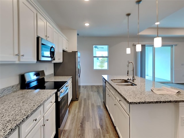 kitchen with appliances with stainless steel finishes, white cabinetry, a center island with sink, and hanging light fixtures