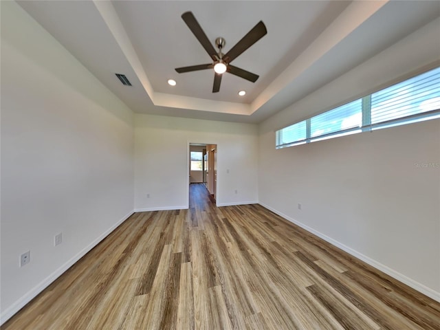 unfurnished room with ceiling fan, a tray ceiling, and light wood-type flooring