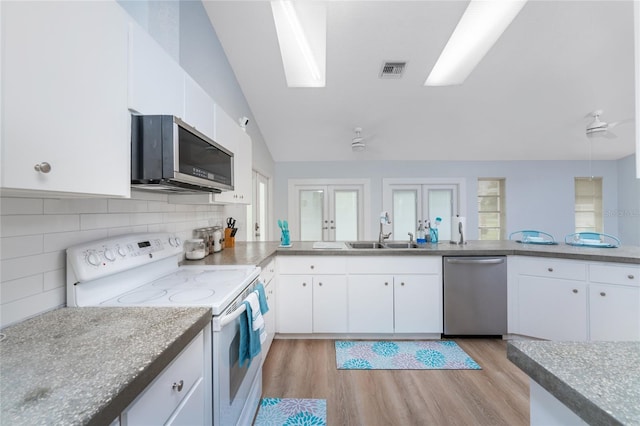 kitchen featuring stainless steel appliances, a sink, visible vents, vaulted ceiling, and light wood-type flooring