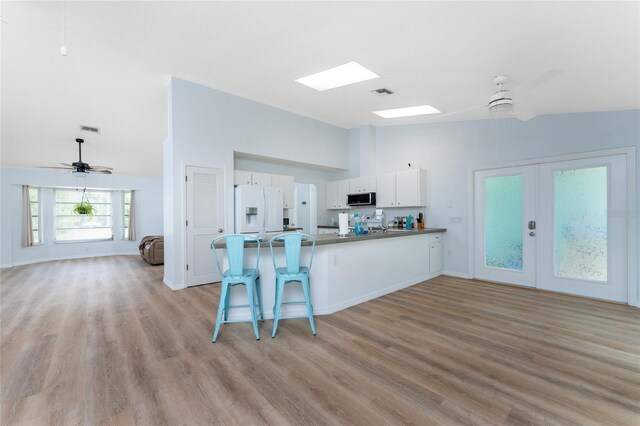 kitchen with a breakfast bar, white fridge with ice dispenser, light hardwood / wood-style flooring, white cabinets, and ceiling fan