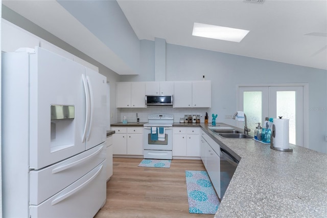 kitchen featuring white appliances, white cabinetry, a sink, and lofted ceiling with skylight