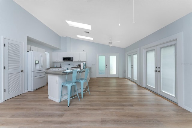 kitchen featuring a breakfast bar, vaulted ceiling with skylight, white appliances, french doors, and white cabinetry