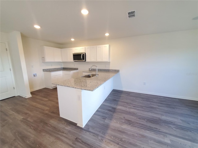 kitchen with sink, dark hardwood / wood-style floors, kitchen peninsula, white cabinets, and light stone countertops