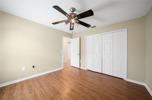 unfurnished bedroom with a closet, visible vents, ceiling fan, wood finished floors, and baseboards