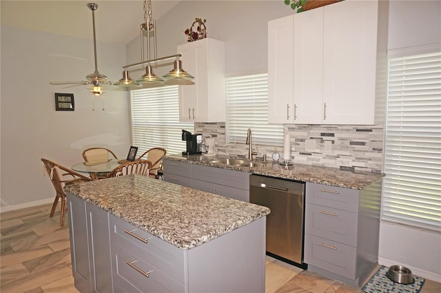 kitchen with lofted ceiling, light stone countertops, stainless steel dishwasher, backsplash, and sink