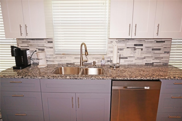 kitchen with sink, stainless steel dishwasher, dark stone counters, and white cabinetry