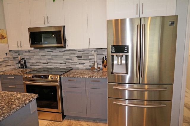 kitchen with appliances with stainless steel finishes, backsplash, dark stone counters, and white cabinetry