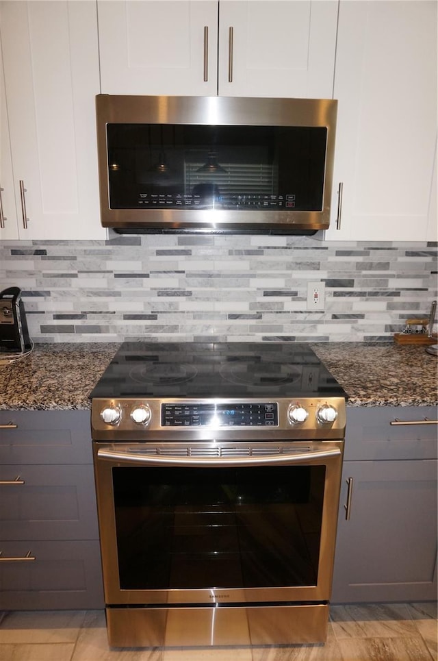 room details with appliances with stainless steel finishes, tasteful backsplash, white cabinetry, and dark stone countertops