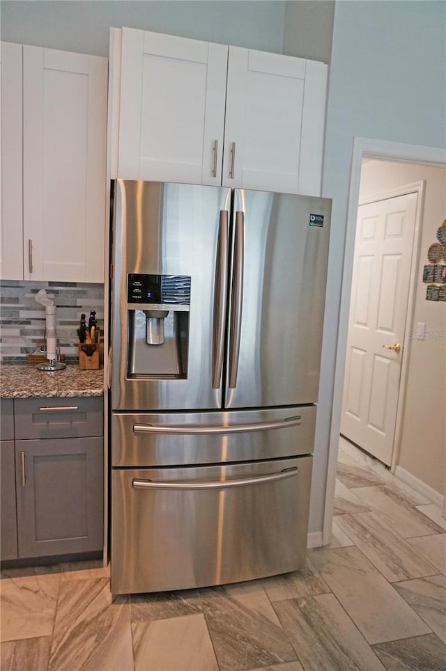 kitchen featuring stainless steel fridge, backsplash, white cabinets, and stone countertops