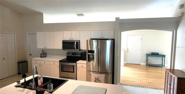 kitchen with arched walkways, light countertops, appliances with stainless steel finishes, light tile patterned flooring, and a sink