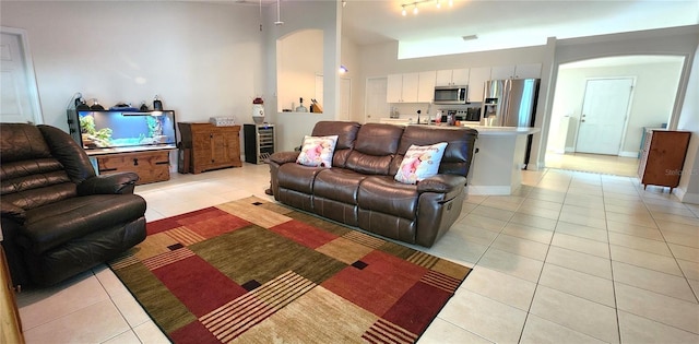 living room featuring light tile patterned floors, baseboards, arched walkways, a towering ceiling, and wine cooler