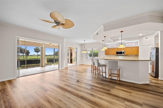 kitchen featuring a kitchen bar, stainless steel appliances, light hardwood / wood-style floors, decorative backsplash, and ceiling fan