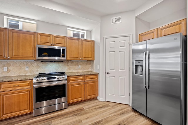 kitchen with decorative backsplash, light stone countertops, stainless steel appliances, and light hardwood / wood-style floors