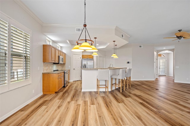 kitchen with a breakfast bar, backsplash, a kitchen island with sink, stainless steel appliances, and light hardwood / wood-style floors